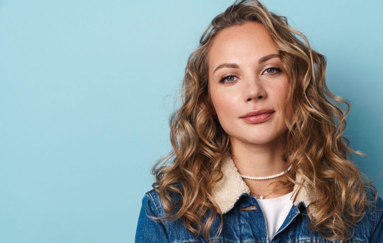 Blonde young woman posing and looking at camera isolated over blue wall