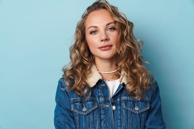 Blonde young woman posing and looking at camera isolated over blue wall